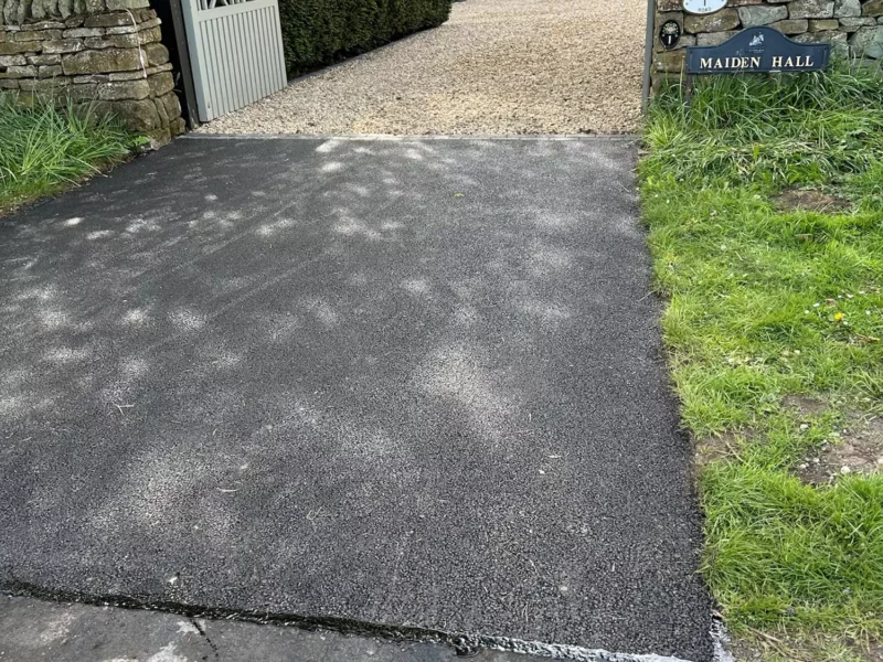 Close up of finished tarmac driveway entrance leading to gravel driveway
