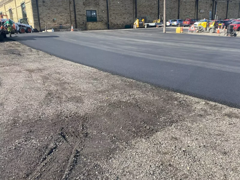 Newly paved tarmac surface in front of a long, stone industrial building