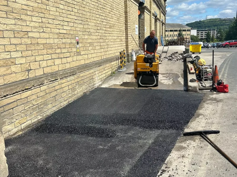 Worker on roller resurfacing tarmac section of a road