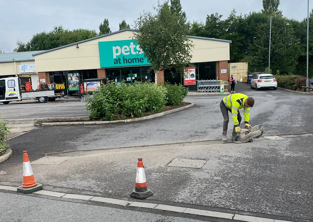 Worker cutting road section with an angle grinder in front of Pets at Home