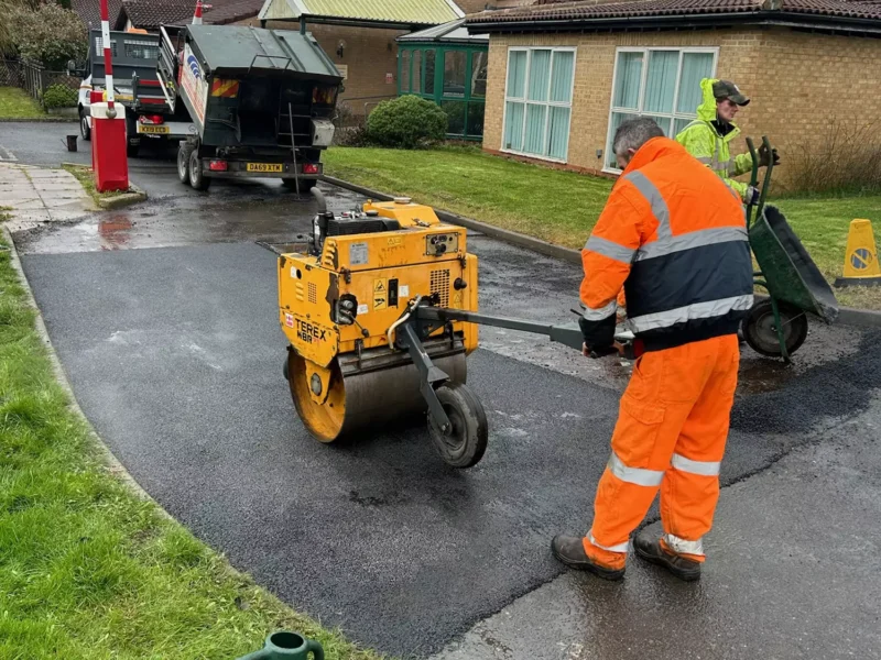 Roller compacting fresh tarmac on a short stretch of road after pothole repair