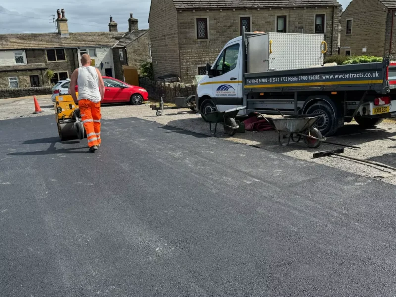 Road paving work in a residential area, showing a worker laying tarmac with a roller